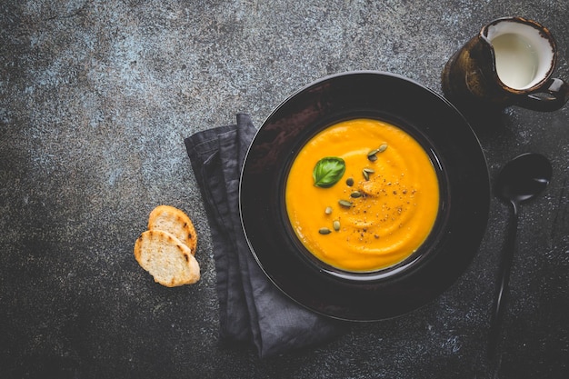 Zuppa di zucca vegetariana autunnale con semi su sfondo scuro, vista dall'alto