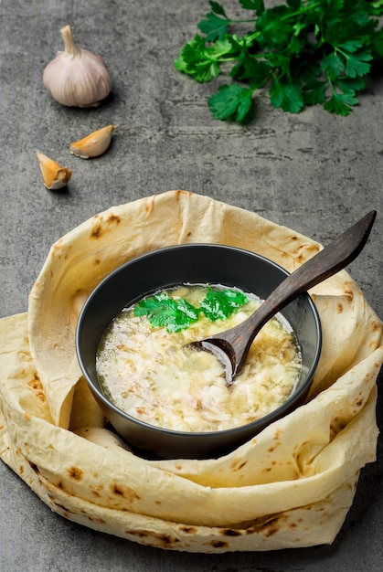 Zuppa khash calda tradizionale in una ciotola, vista dall'alto. Piatto orientale tradizionale armeno, turco o caucasico - khash, con coriandolo fresco, aglio e pane lavash essiccato