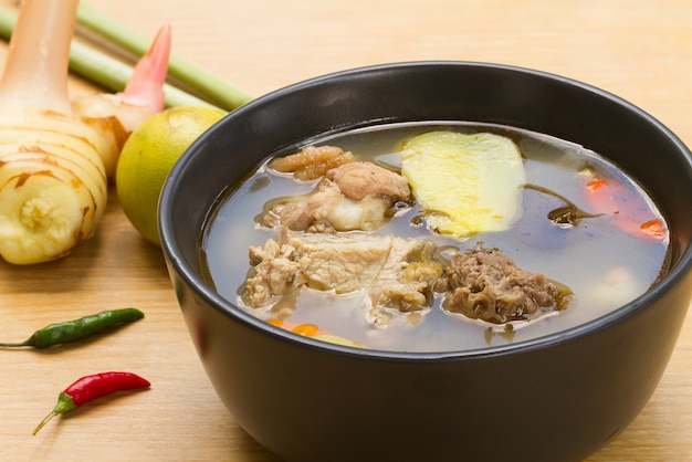 Zuppa piccante e aspro con pollo e foglia di tamarindo giovane In una tazza bianca su un tavolo di legno.