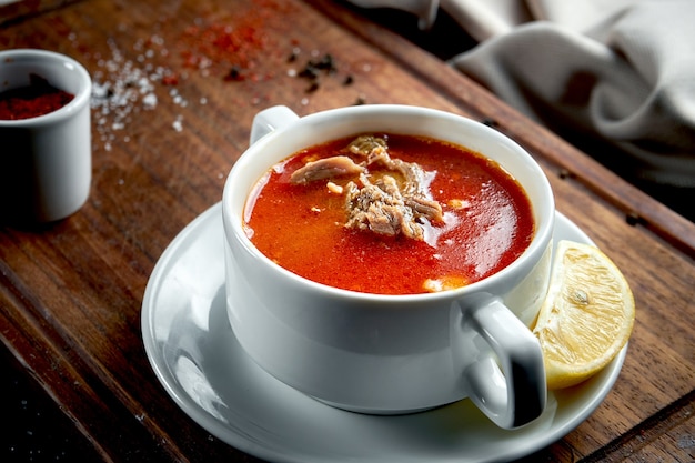 Zuppa turca rossa con agnello e verdure in un piatto bianco su un vassoio di legno. Tavolo scuro