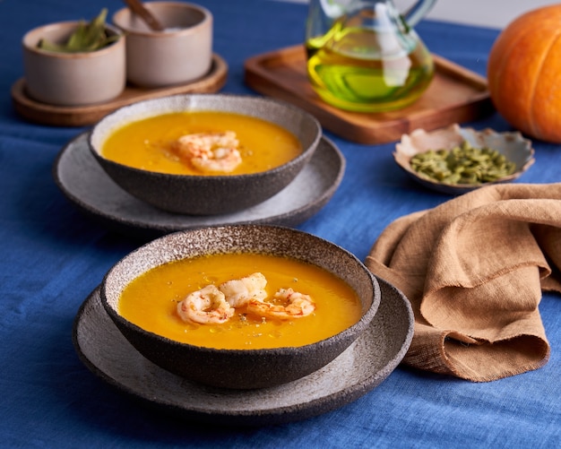 Zuppa vegetariana di purea di crema di zucca e carote con gamberi e semi in una ciotola sul tavolo di lino blu