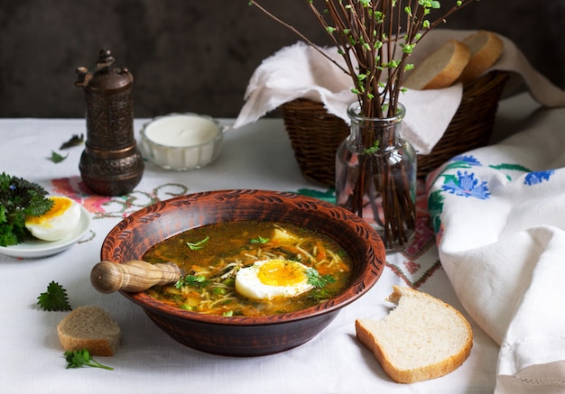 Zuppa verde di primavera con erbe, verdure e piselli, servita con uova e panna acida. Stile rustico.