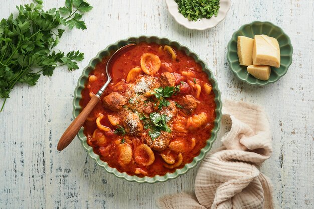 Zuppa Zuppa di pomodoro fresco con polpette di pasta, verdure e prezzemolo in una ciotola rustica verde su fondo di legno Cucina tradizionale italiana Cena sana mangiare Vista dall'alto Concetto di cena accogliente autunnale