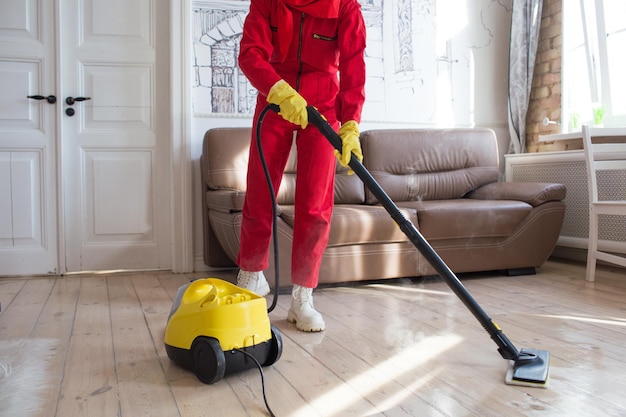 A cleaner in a red uniform cleans the floor with the help of steam coming out of the nozzle