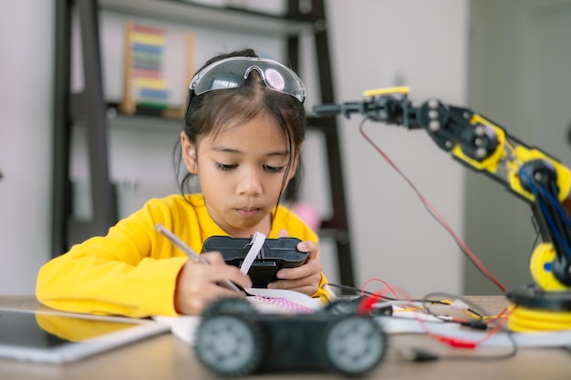 A young girl is sitting at a table with a robot and a remote control