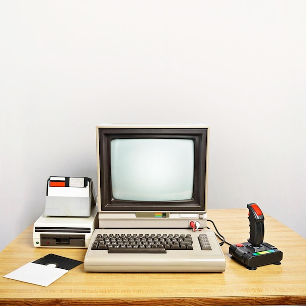 an old computer on a desk with joystick and floppy disks blank screen insert your own message large