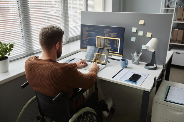 Back view man with disability using wheelchair and coding in it development