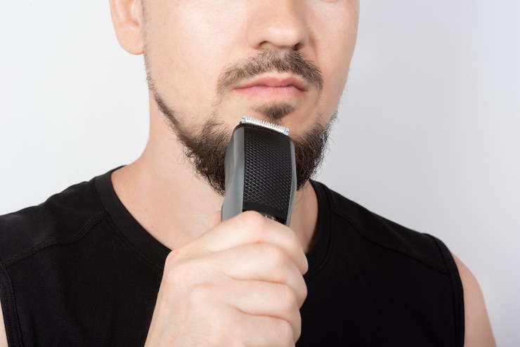 Fotografie bearded man holding a trimmer in his hand closeup