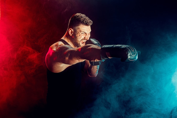 Fotografie bearded tattooed sportsman muay thai boxer in black undershirt and boxing gloves fighting on dark wall with smoke. sport concept.