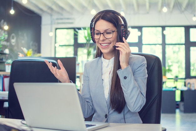 Beautiful friendly call center agent woman with headset using laptop and talking to a client via online customer support service