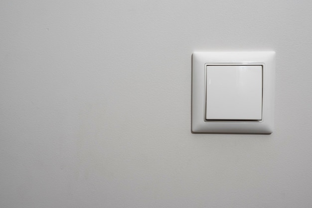 Bílý vypínač, plastový mechanický vypínač bílé barvy instalovaný na světle šedé zdi