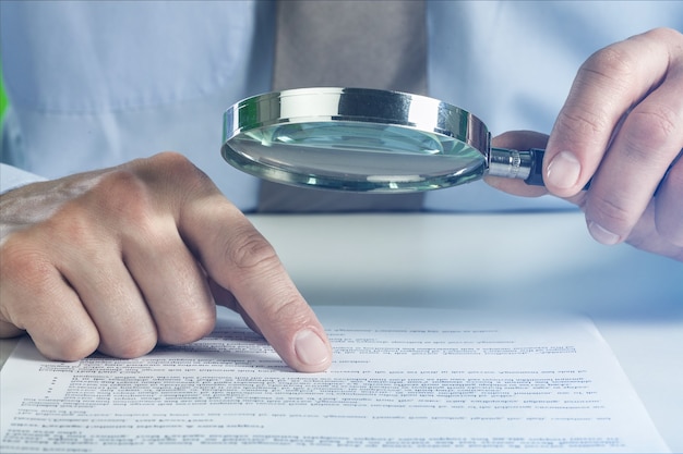 Business analytics and statistics. Businessman with report using a magnifying glass.