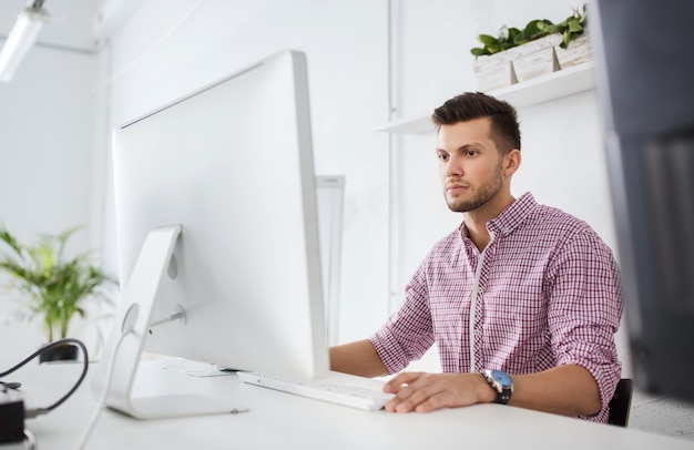 business, technology, education and people concept - young creative man or student with computer at office