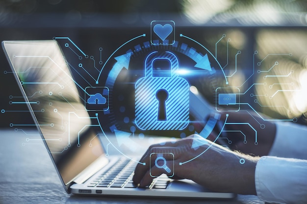Close up of businessman hands using laptop on desktop with abstract glowing blue padlock hologram on blurry background Internet information technology and security concept Double exposure