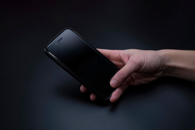 close-up of hand using blank mobile phone over black background