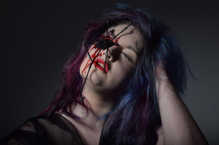 Fotografie close-up of woman with spider and blood on face against black background