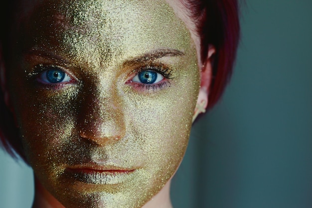 Close-up portrait of woman face with golden paint against green background