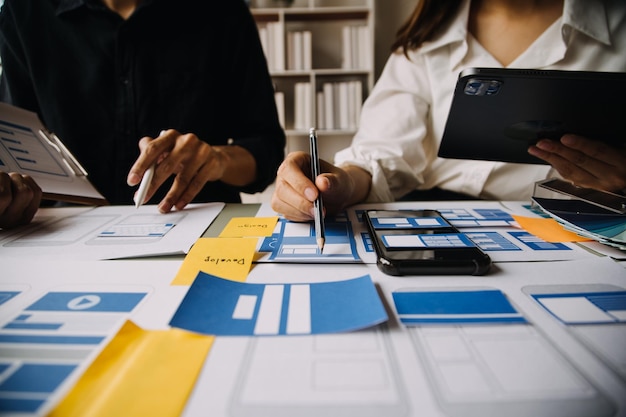 close up ux developer and ui designer brainstorming about mobile app interface wireframe design on table with customer breif and color code at modern officecreative digital development agency