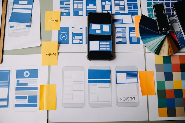 Close up ux developer and ui designer brainstorming about mobile app interface wireframe design on table with customer breif and color code at modern officeCreative digital development agency