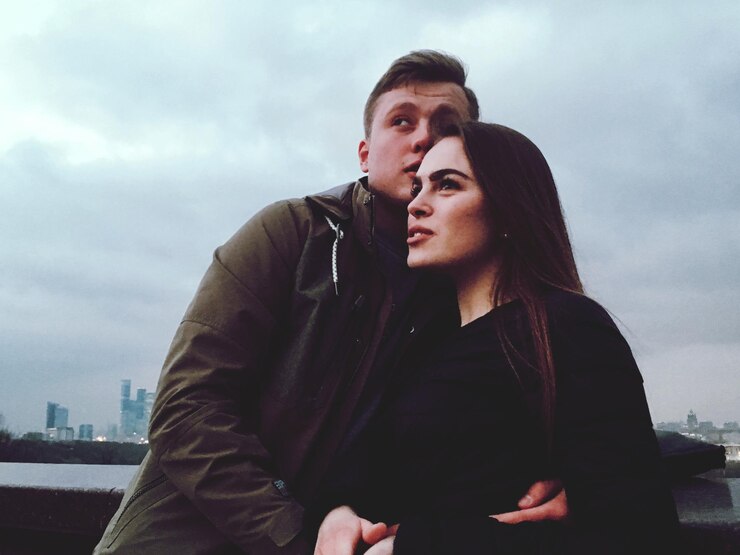 Fotografie couple looking away while standing by retaining wall against cloudy sky