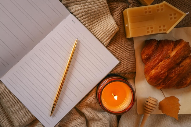 cozy flat lay with open notebook golden pen candle honey dipper croissant and decorative beeswax house on warm knit fabric autumninspired journaling scene