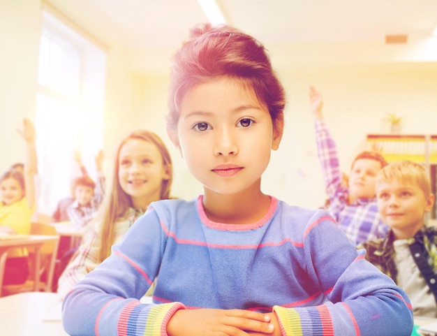 education, elementary school and children concept - little student girl over classroom and classmates background