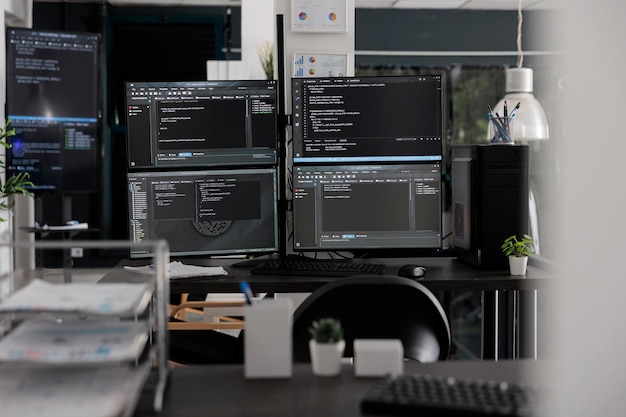 Empty it office with computer screens on desk, computers in background running programming code and algorithms on terminal window. Firewall network servers in software company.