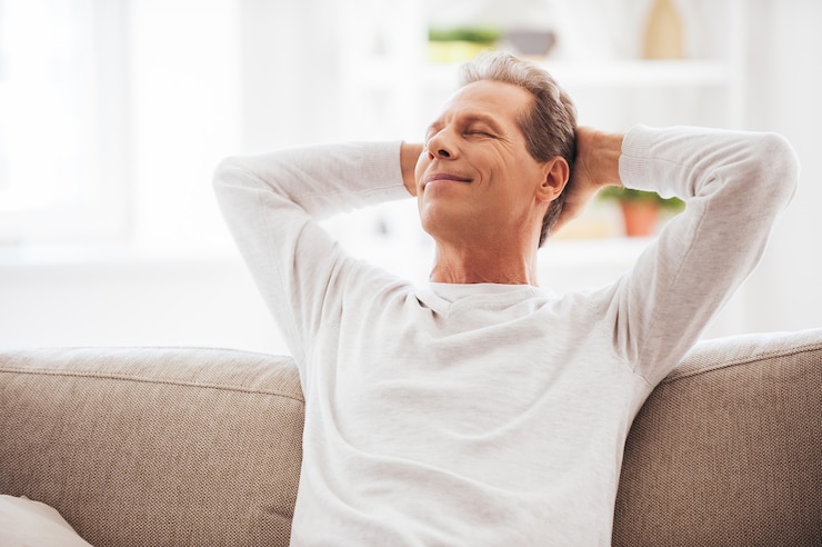Fotografie enjoying free time at home. cheerful mature man holding hands behind head and looking relaxed while sitting on the couch at home