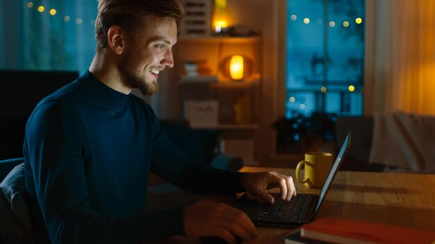 Evening at Home Portrait of Handsome Man Sitting at His Desk Working on a Laptop Smiling Freelancer Working on Computer Side View Shot