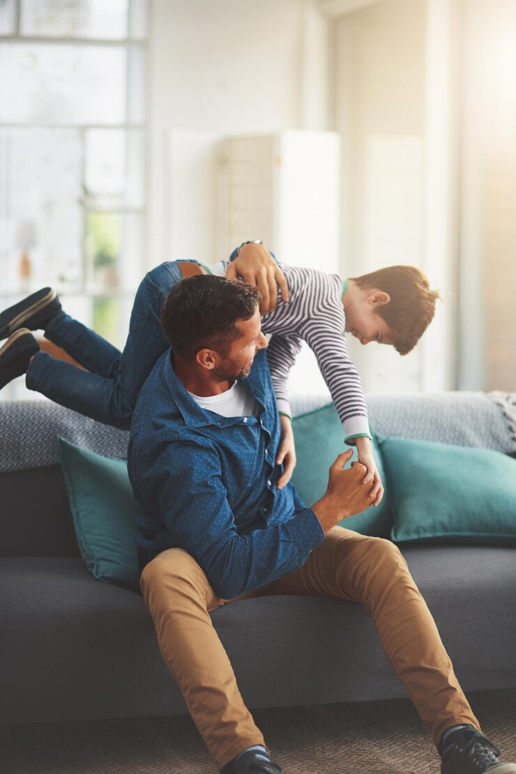 Fotografie father boy and playing on sofa together in home bonding and support for communication or care daddy son and family wrestling games in living room talk and embrace for security in relationship