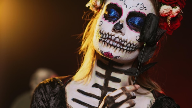 glamorous goddess wearing death costume and flowers wreath over studio background, acting like holy santa muerte. la cavalera catrina lady of dead with skull body art, mexican culture. handheld shot.