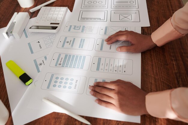Hands of ux designer leaning on table with layouts of new mobile application interface