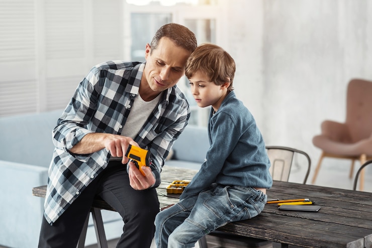 Fotografie happy child. handsome joyful dark-haired man showing instruments to his son while sitting on the table and his son sitting near him