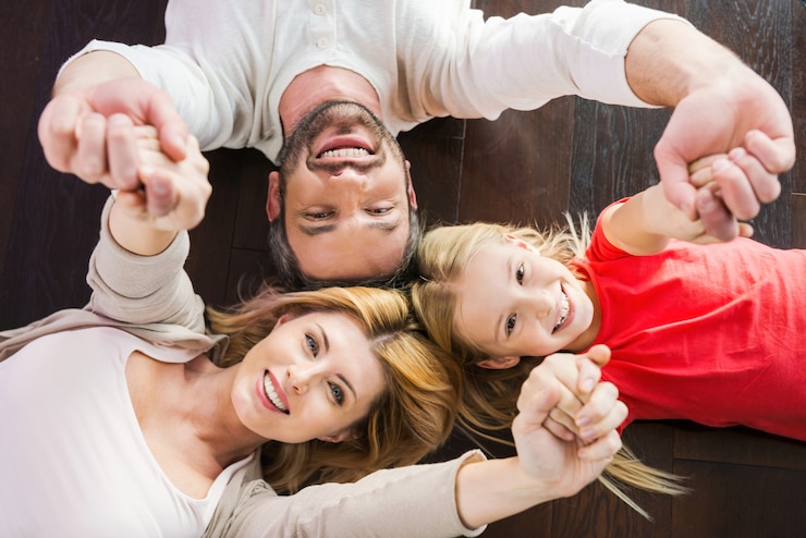 Fotografie happy family together. top view of happy family of three bonding to each other and smiling while lying on the hardwood floor