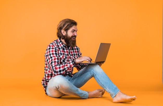 happy handsome bearded guy with unshaven face and stylish hairdo wear casual clothes working on notebook freelance