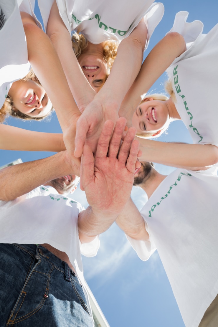 Fotografie happy volunteers with hands together against blue sky
