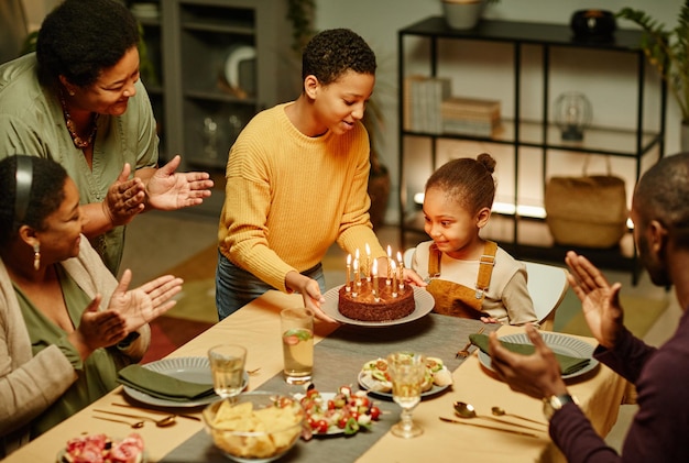 high angle portrait of smiling teenage boy bringing birthday cake to little sister celebrating holid...