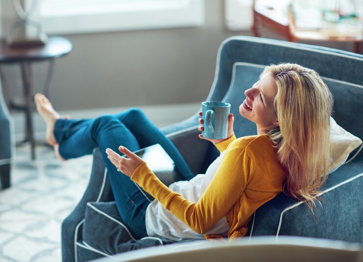 Fotografie house tablet and woman on couch coffee and rest in living room morning and happy with social media relax calm and girl with break smile or peace in lounge cozy and person with tea in apartment