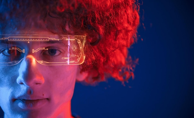 in futuristic eyewear young man with curly hair is indoors illuminated by neon lighting