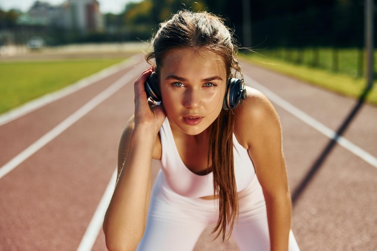 Fotografie listening to the music in headphones young woman in sportive clothes is exercising outdoors