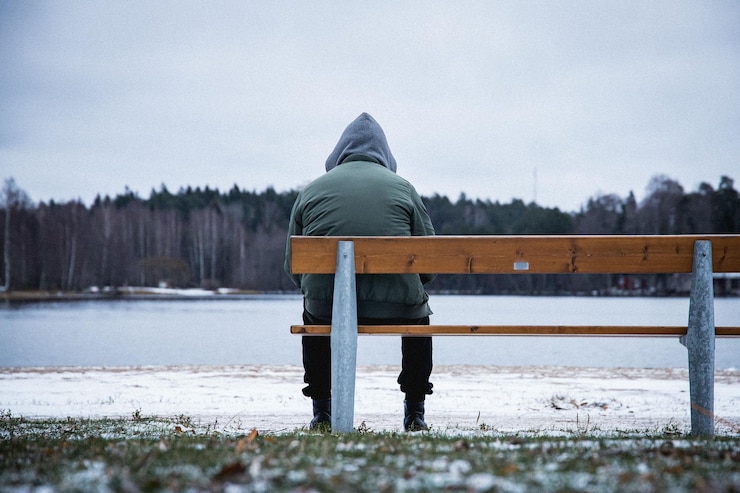 Fotografie lonely man sitting on the bench in a snowy park