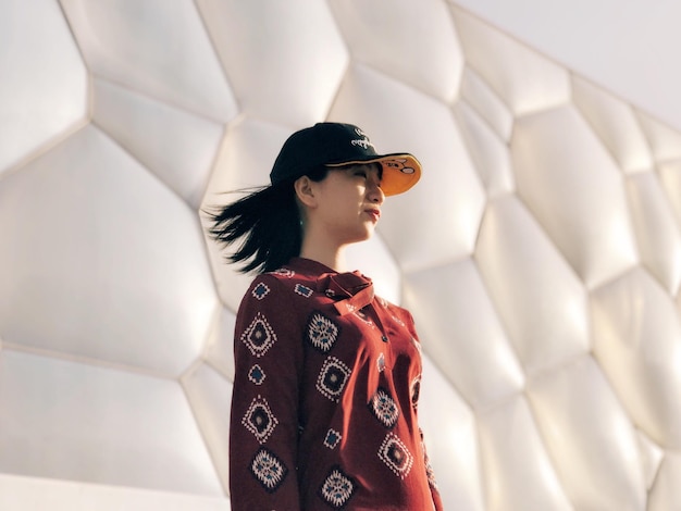 low angle view of young woman looking away while standing against patterned wall