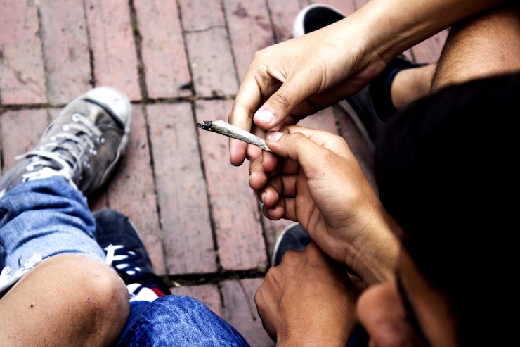 Fotografie low section of male friends smoking marijuana joint while sitting outdoors
