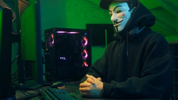 Lviv Ukraine June 03 2024 Masked man anonymous stretching fingers programmer hacking typing computer malware networks web danger scam database spy system virus theft server break cryptocurrency