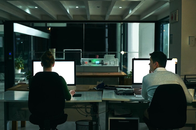 making success happen at all hours of the day and night rearview shot of two businesspeople working on computers in an office at night