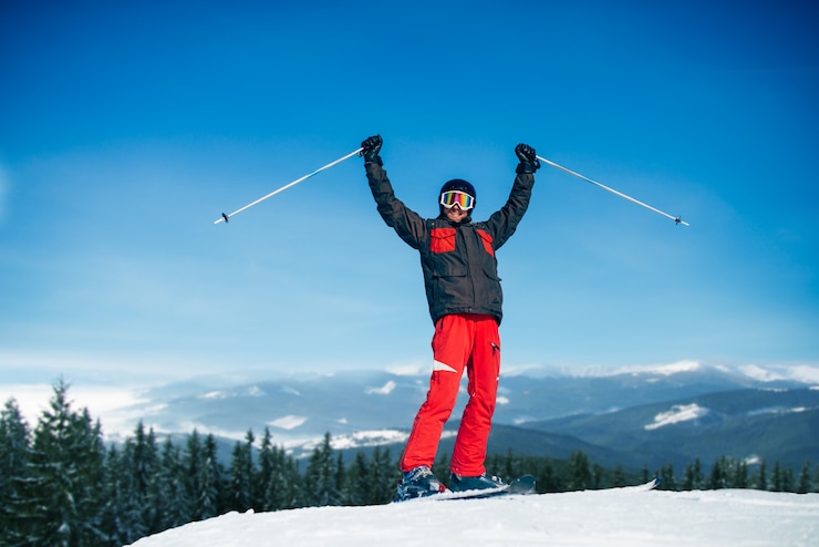 Fotografie male skier hands up on the top of mountain, blue sky, forest and snowy mountains. winter active sport, extreme lifestyle. downhill skiing