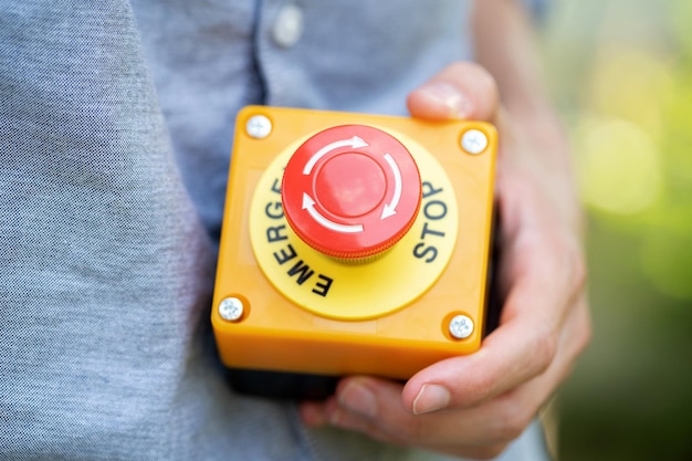 Man holding a large red industrial machinery emergency stop button in hand object closeup detail workplace occupational safety security rules laws and policies OHS work accidents simple concept