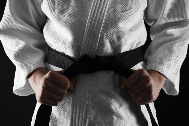 Fotografie man in keikogi tying black belt on dark background closeup martial arts uniform