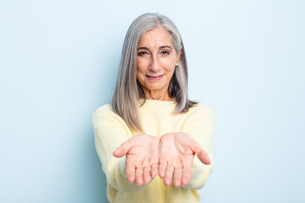 middle age gray hair woman smiling happily with friendly, confident, positive look, offering and showing an object or concept