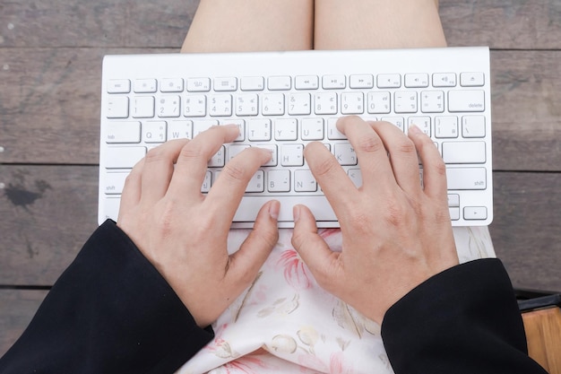 Midsection of woman typing while sitting on wooden floor